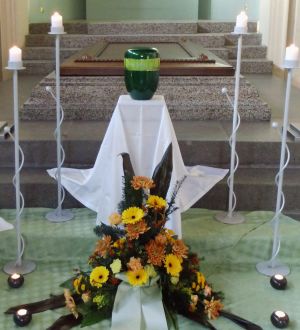 Blumenschmuck aus gelben Blüten mit grüner Urne für eine Urnenbeisetzung Blumenschmuck aus gelben Blüten mit grüner Urne für eine Urnenbeisetzung