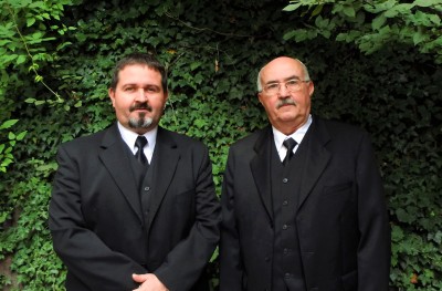 im Bild Martin (li.) und Wolf von Chamier in schwarzen Anzügen imHintergrund eine Hecke